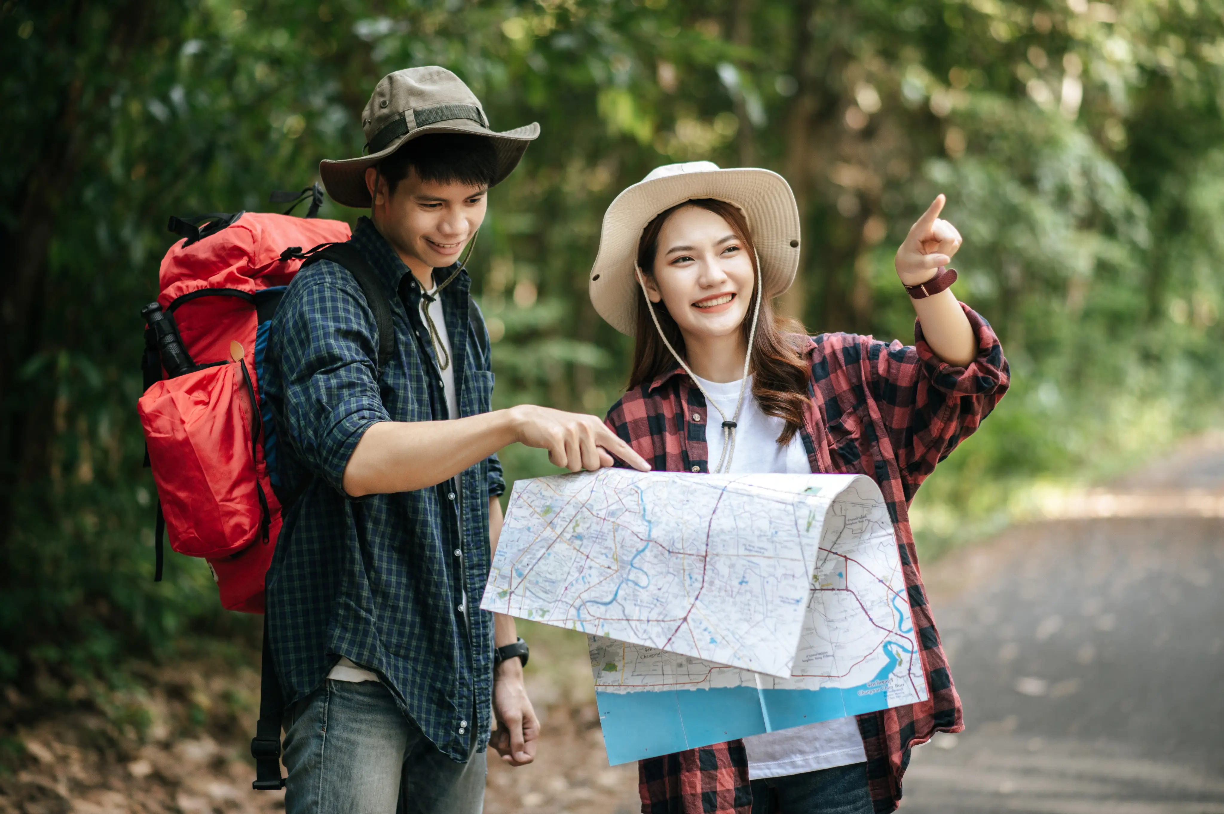 Two hikers with hats holding and examining a map in a forested area.